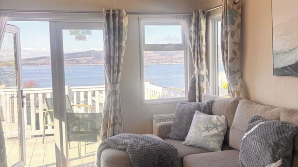 Et værelse med en sofa, udsigt til vand og en balkon med stole.