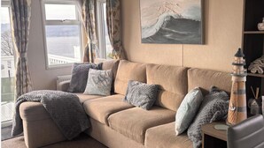 En beige sofa med flere puder, et maleri af en bølge, et fyrtårn og udsigt til bybiler gennem et vindue.