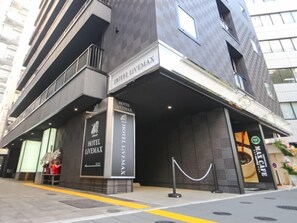 A modern hotel entrance with a prominent sign for Hotel Livemax, a gated entrance, and a coffee shop visible to the right. - Hotel Livemax Yokohama Station West Exit (Yokohama)