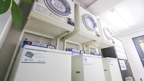 A row of stacked washing machines in a room with a door on the right. - Hotel Livemax Yokohama Station West Exit (Yokohama)