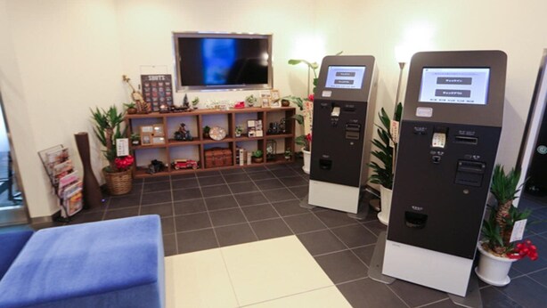 A reception area with a television, two self-service kiosks, a sofa, and a shelf with various items. - Hotel Livemax Yokohama Station West Exit (Yokohama)