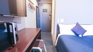 A hotel room with a bed, a desk with a television, a door, and a wall-mounted light switch. - Hotel Livemax Yokohama Station West Exit (Yokohama)