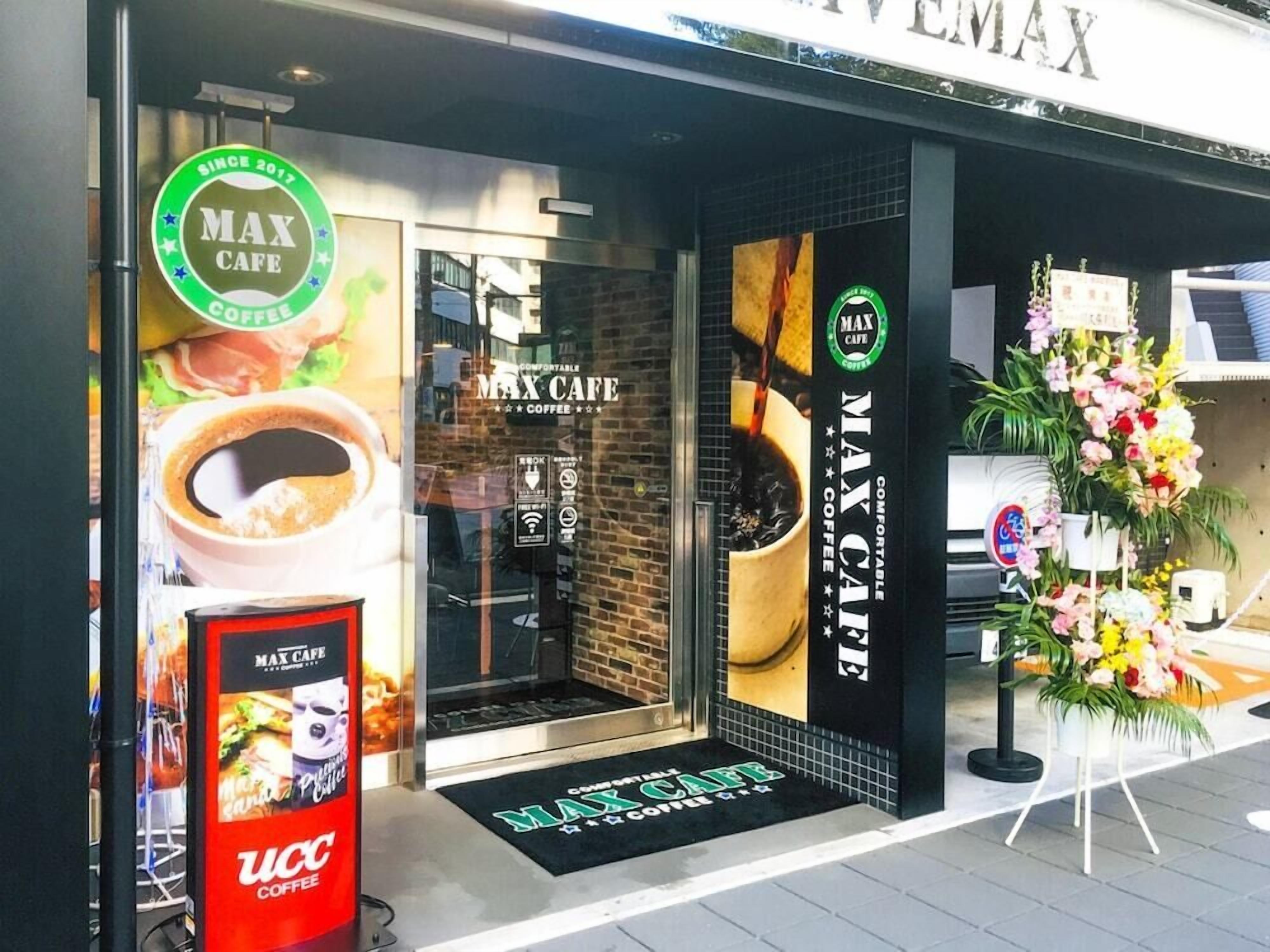 A coffee shop entrance with a sign reading 'Max Cafe' and a flower arrangement outside.