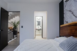 Une chambre à coucher avec un lit, une tête de lit en bois, un mur en marbre, un escalier et une salle de bain visible à travers une porte ouverte.