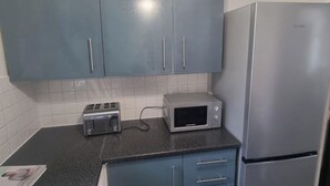 A kitchen with blue cabinets, a toaster, a microwave, and a refrigerator. - East London 2-Bed Ap Sleeps 4 near Hainault Forest (Romford)