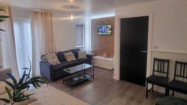 A living room with a sofa, coffee table, TV, and a door. - East London 2-Bed Ap Sleeps 4 near Hainault Forest (Romford)