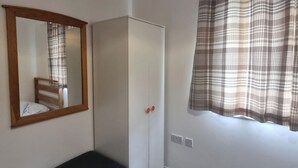 A room with a wardrobe, a bench, a mirror, and a window with a plaid curtain. - East London 2-Bed Ap Sleeps 4 near Hainault Forest (Romford)