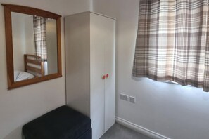 A room with a wardrobe, a bench, a mirror, and a window with a plaid curtain. - East London 2-Bed Ap Sleeps 4 near Hainault Forest (Romford)