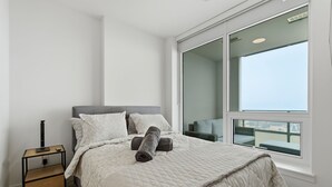 Un dormitorio con cama, mesita de noche, ventana con vistas y balcón.