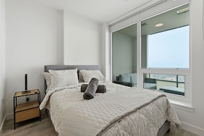Ein Schlafzimmer mit einem Bett, einem Nachttisch, einem Fenster mit Blick und einem Balkon.