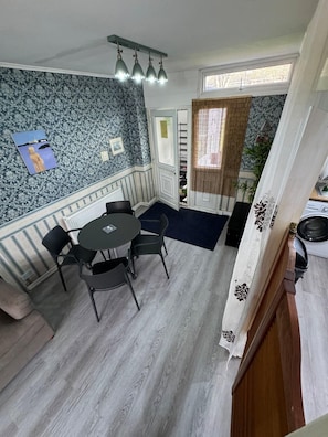 A room with a dining table, chairs, a kitchen area, a patterned wall, and a window with curtains. - House Of Comfort in London (Greater London)