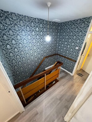 A room with a patterned wallpaper, a wooden staircase, and a light fixture.