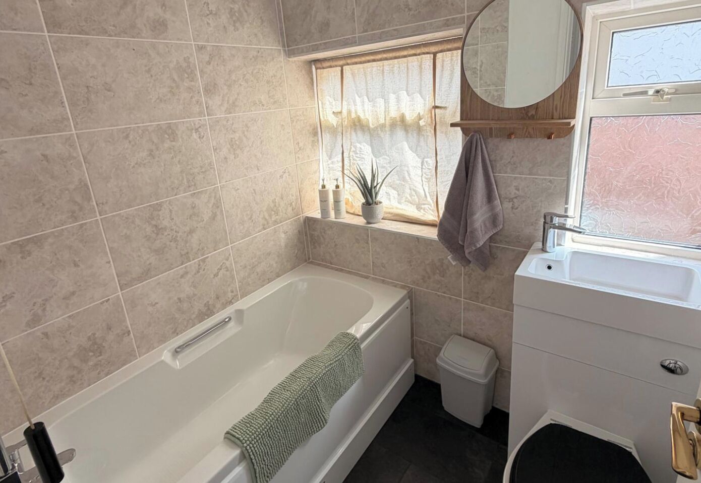 Une salle de bain comprenant une baignoire, des toilettes, un lavabo, une fenêtre avec un rideau et un miroir.