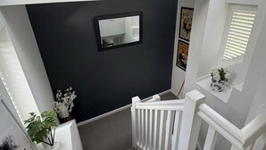 Un escalier avec un mur sombre, une rampe blanche et une petite fenêtre ornée d’une plante.
