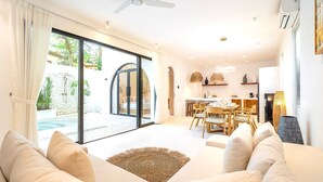 A modern living room with a sofa, a dining area, and a view of a swimming pool. - Casa Myla Villa - Bingin Bali (Munggu)
