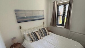 Une chambre à coucher avec un lit, un tableau, une fenêtre avec des rideaux, une table de chevet et une lampe.