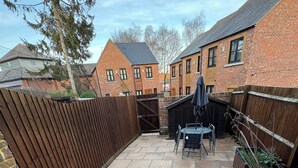 Une cour avec une table et des chaises de patio, une clôture en bois et, au fond, des bâtiments en briques.