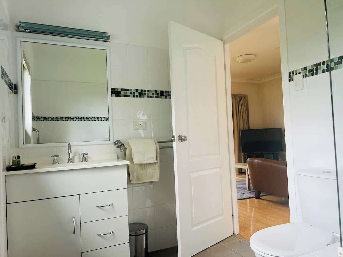 A bathroom with a toilet, sink, mirror, and a towel rack.
