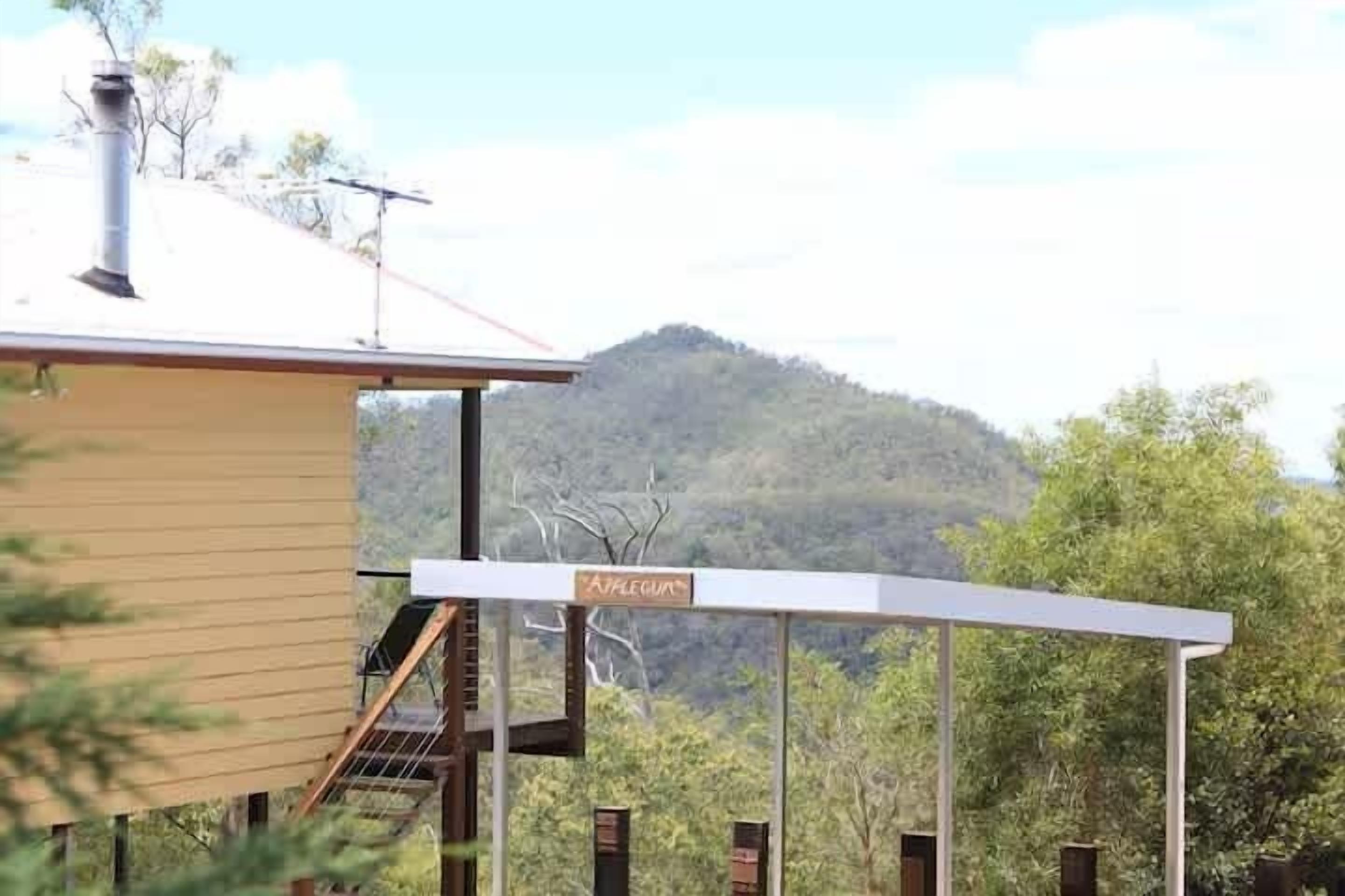 A building with a covered outdoor area, a sign reading 'AFLEGUAR,' and a mountainous backdrop.