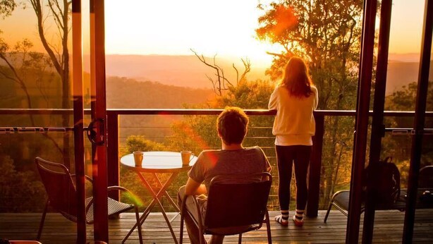 A balcony with a table and chairs, overlooking a landscape with trees and hills.