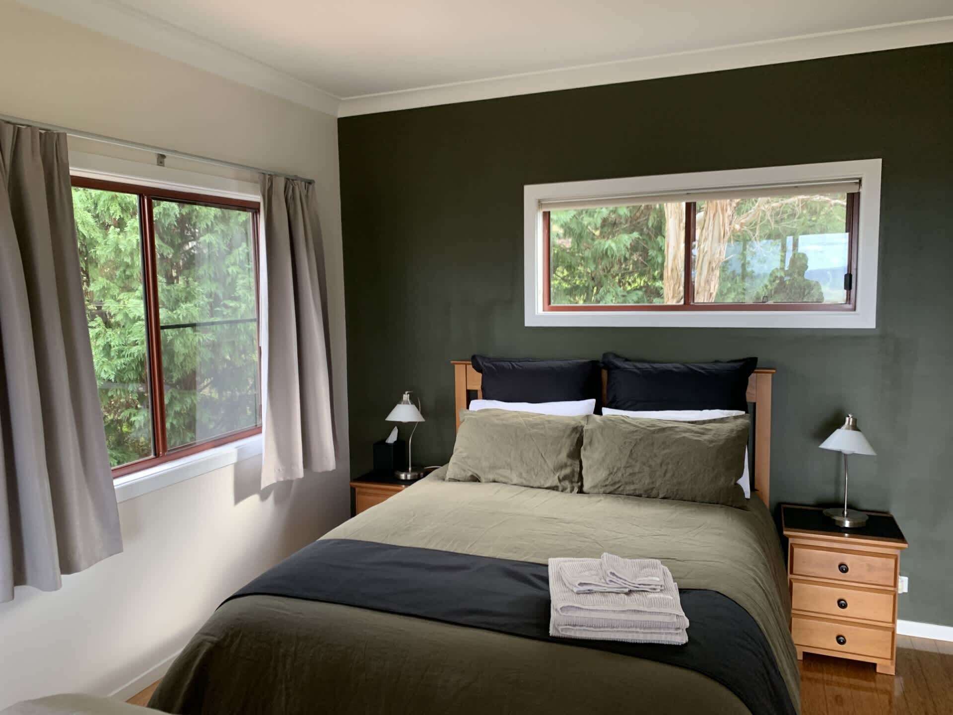 A bedroom with a bed, two bedside tables, a window with curtains, and a view of trees.