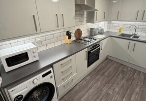Eine moderne Küche mit weißen Schränken, einer Mikrowelle, einem Gasherd, einem Backofen und einer Waschmaschine.