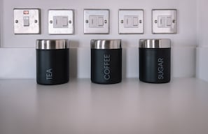 Three cylindrical containers labeled 'TEA,' 'COFFEE,' and 'SUGAR' on a white surface, with a row of light switches above them. - Apartment Sleeps 5 with Air Conditioning (Birmingham)