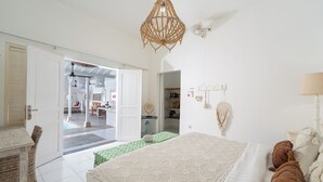 Un dormitorio con una cama, un tapete verde, una pared blanca, un ventilador de techo y una puerta que da a un balcón.