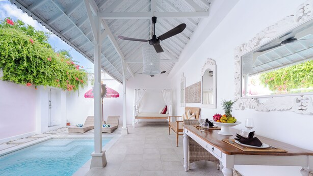 Un área junto a la piscina con un ventilador de techo, una mesa de comedor con frutero y vistas a la piscina.