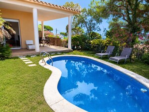 Una piscina con bordo curvo, circondata da un prato curato e un patio coperto con mobili da esterno.