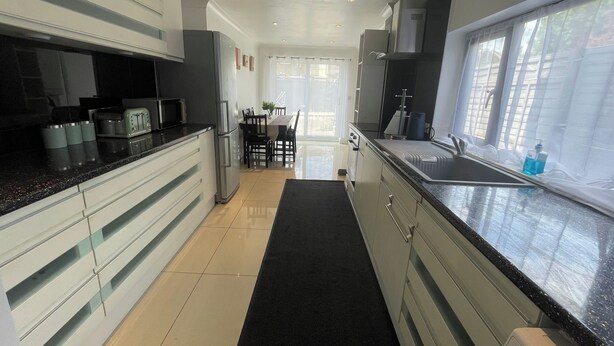 A modern kitchen with a black countertop, stainless steel appliances, and a dining area with a table and chairs. - Tottenham - Sleeps 10 - Garden - Near Transport (London)