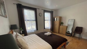 A bedroom with a bed, a wardrobe, a mirror, and a chair. - Tottenham - Sleeps 10 - Garden - Near Transport (London)