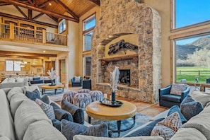 A spacious living area with a stone fireplace, high ceilings, and a view of the outdoors. - Abode at Trail Creek Canyon, views, hot tub, games (Oakley)