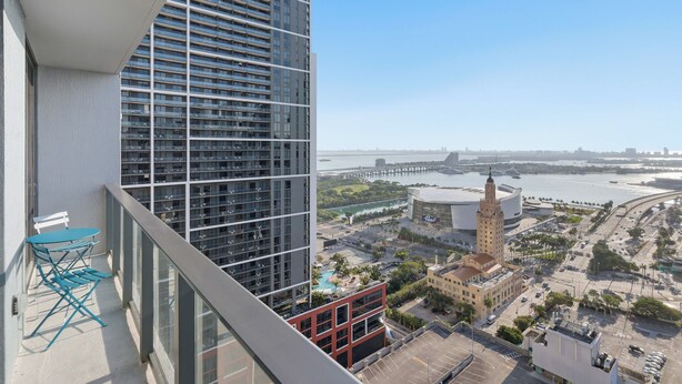 Un edificio alto con un balcón que tiene una mesa y sillas, vista a un río, un puente y una torre distintiva.