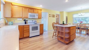 Una cocina con armarios de madera, microondas, horno y un comedor con sillas y mesa.