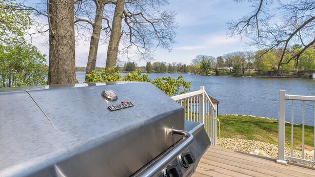 Una parrilla en una terraza con vistas a un lago rodeado de árboles y una barandilla blanca.