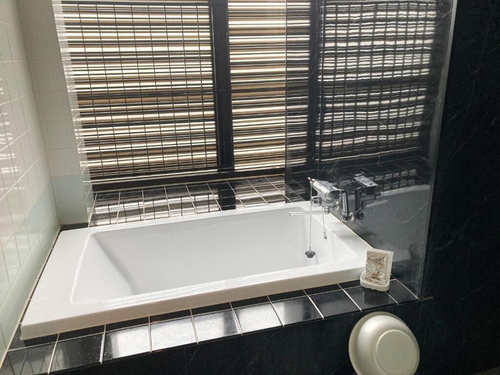 Uma casa de banho com uma banheira grande, uma torneira e uma janela com persianas.