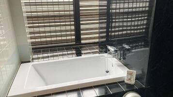 Un baño con una bañera grande, un grifo y una ventana con persianas.