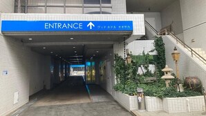 An entrance to a building with a blue sign indicating the direction to the entrance. - GOOD HOTEL OSAKA (Toyonaka)