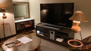 A hotel room with a flat-screen TV, a wooden coffee table, a desk with a chair, and a lamp. - GOOD HOTEL OSAKA (Toyonaka)