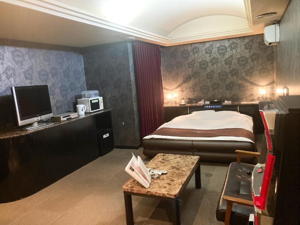 Une chambre d’hôtel avec un lit, un bureau avec une télévision, un four à micro-ondes et une petite table avec un magazine.