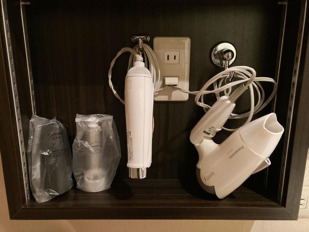 A dark wooden cabinet with a power outlet, a white device with a cord, and two plastic bags.