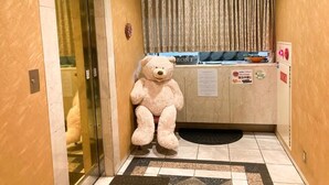 A hotel reception area with a large teddy bear, a reception desk, and a sign indicating the direction to the elevator. - GOOD HOTEL OSAKA (Toyonaka)