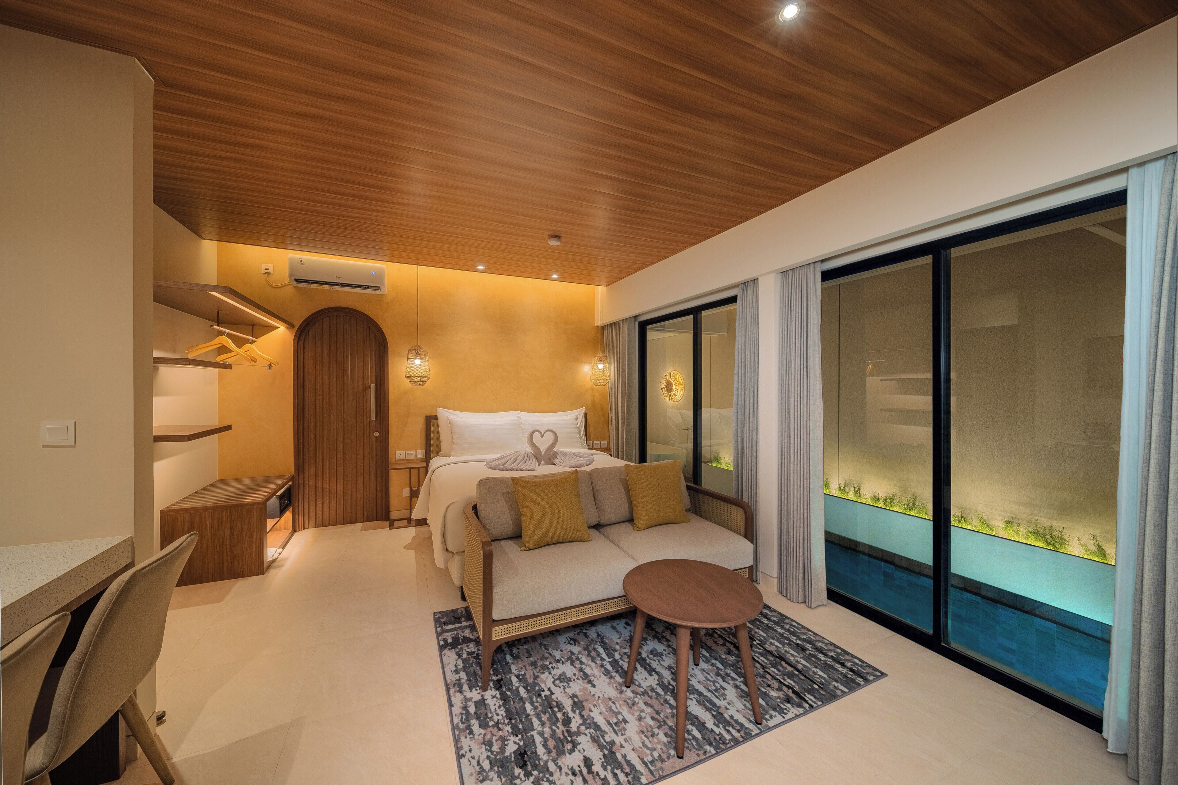 A modern hotel room with a bed, a sofa, a desk, and a large window with a view.