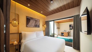 Una habitación de hotel moderna con una cama grande, un escritorio, una silla, una mesita pequeña, una lámpara colgante y vistas a una piscina.