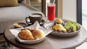 Una mesa de comedor con un plato de comida, un vaso de bebida roja y una taza de café.