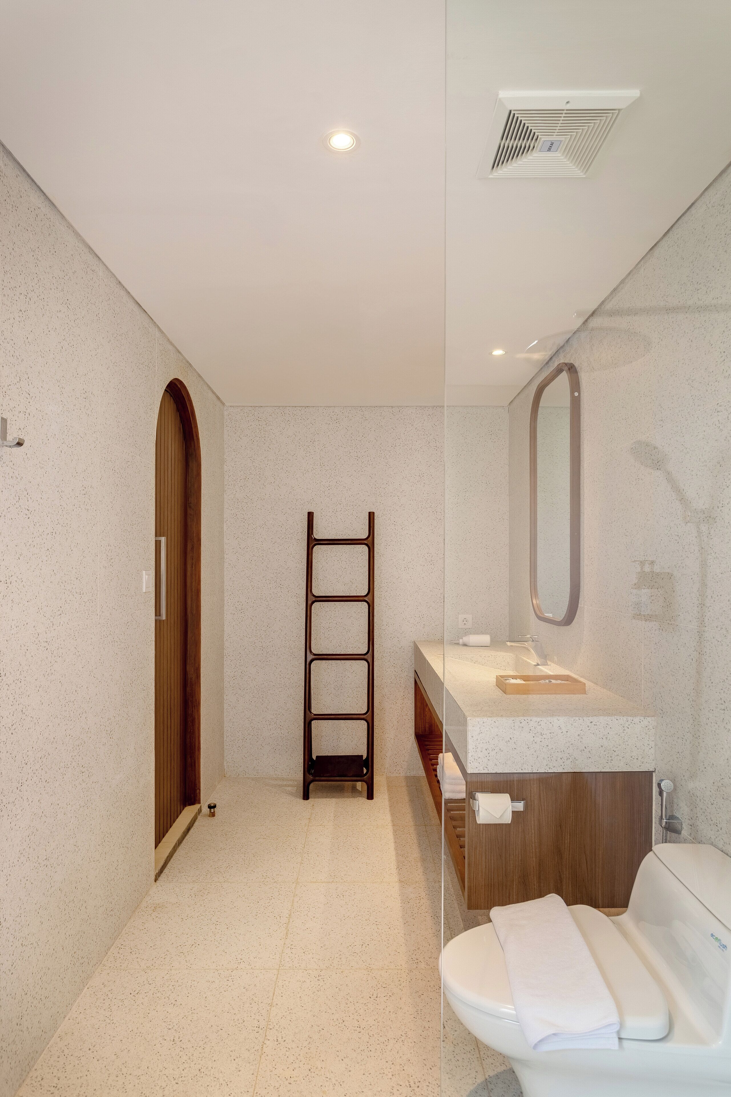 Un baño moderno con separador de vidrio, escalera de madera, lavamanos con espejo e inodoro.