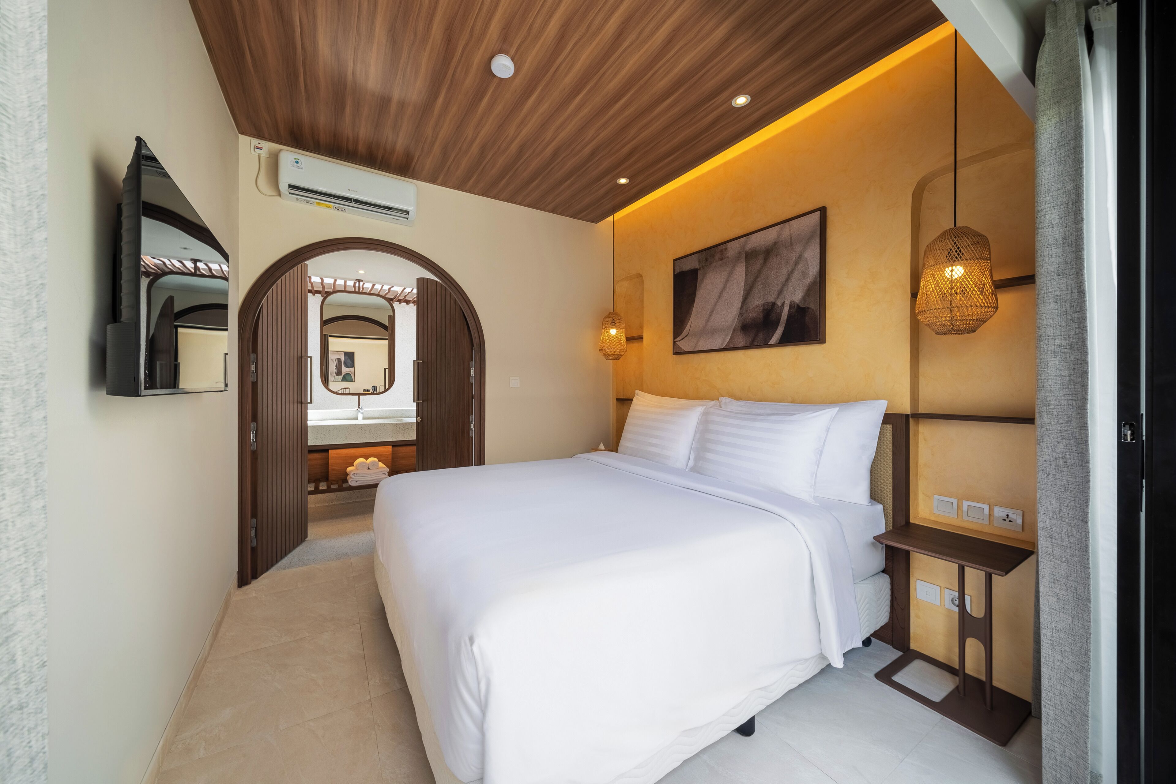 A bedroom with a bed, bedside table, wall-mounted air conditioner, and a mirror.