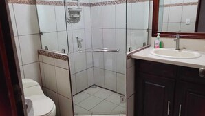 Een badkamer in hoekopstelling met een douchecabine van glas, een toilet, een wastafel en donkere houten kastjes.