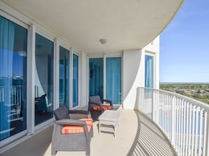 Ein Balkon mit Korbmöbeln, großen Fenstern mit blauen Vorhängen und einem weißen Geländer.